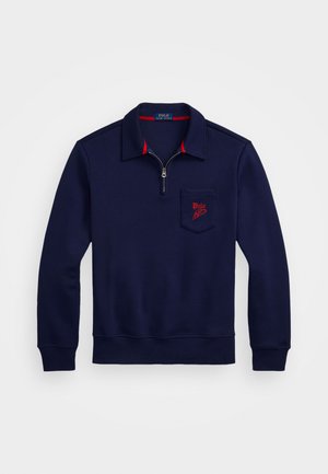 Suéter azul marino con cuello de media cremallera, acentos rojos en el escote y un bolsillo en el pecho izquierdo con un logo bordado. Material suave.