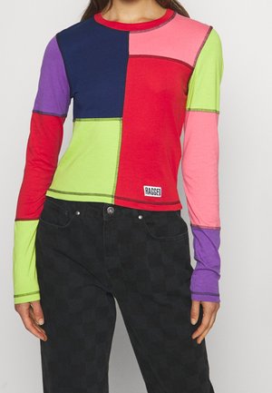 Haut patchwork à manches longues avec des blocs de couleur en marine, rouge, rose, vert citron et violet, assorti à un pantalon à carreaux noir.
