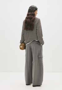 Maglia a maniche lunghe a righe marroni e bianche, abbinata a pantaloni cargo grigi larghi con tasche laterali e una piccola borsa marrone.
