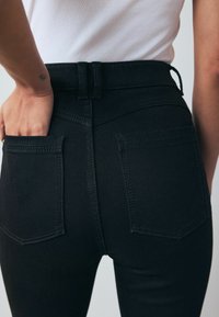 Black high-waisted jeans with visible back pockets, textured denim fabric, and stitched detailing along the waistband and pockets.