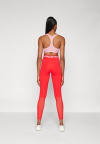 Sportowy strój zawierający różowy top sportowy i czerwone legginsy z wysokim stanem, wyposażone w siateczkowe wstawki oraz biały logo "PRO" na pasku.