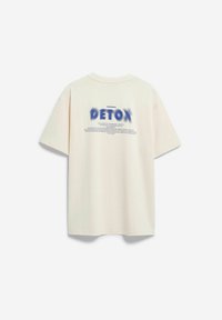 Roomkleurig oversized katoenen t-shirt met "DETOX" in blauwe verloopletters op de achterkant, met extra tekst eronder.