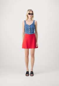 Farmer cropped top gombokkal, piros pöttyös szoknyával párosítva. Fekete nyitott orrú szandálok. A modellen hosszú szőke haja van és napszemüveget visel.