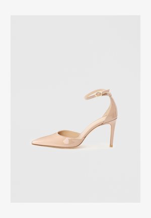 Shoe de verniz nude com biqueira pontuda, tirante no tornozelo e tacão agulha, apresentando uma textura suave e design minimalista.