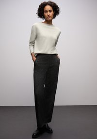 Světle šedý svetr se širokým výstřihem a dlouhými rukávy, doplněný tmavými texturovanými kalhotami s rovným střihem a kapsami. Černé kotníkové boty.