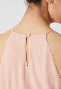 Rožinė šifono palaidinė su skylute nugaroje, turi plonas petnešas ir mažą audiniu aptrauktą sagutę.