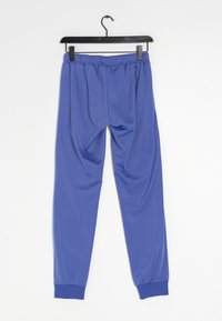 Blå träningsbyxor i glatthudigt, lätt tyg. Har en elastisk midja och tighta manschetter vid anklarna, hängande från en svart krok.