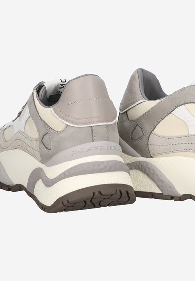 Sneaker con una toma superiore in suede e pelle grigia e beige miscelati, dotate di una robusta suola bianca, dettagli testurizzati e logo sul tallone.