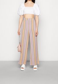 Färgglada vida byxor med ett zigzag-mönster i rosa, gult och grönt. Kombineras med en vit kortärmad crop top och platåsandaler.