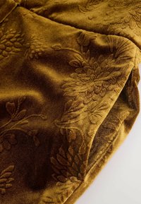 Tela de terciopelo dorado con un patrón floral en relieve, que presenta una textura suave y un color intenso. El detalle en la superficie añade profundidad.