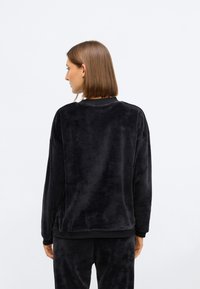 Sweatshirt de veludo preto com uma textura suave, decote redondo, mangas longas e bainha canelada. Projetado com um corte relaxado para maior conforto.