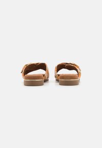 Back view of sandals featuring a floral patterned upper, suede material, light brown base, and a low block heel with gold accents.