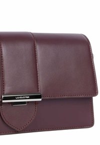 Donkerbruine leren clutch met zilveren sluiting van het merk Lancaster op de voorflap, zichtbare stiksels langs de randen.