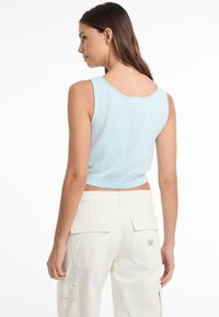 Top corto azzurro chiaro con orlo a coste, abbinato a pantaloni cargo crema con tasche laterali e un'etichetta sul retro.