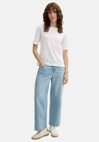Witte top met korte mouwen en een ronde halslijn, gecombineerd met lichtblauwe wijde jeans en witte sneakers met beige accenten.