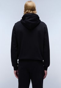 Black hoodie with a soft texture, featuring a kangaroo pocket and a drawstring hood. Paired with matching black pants.