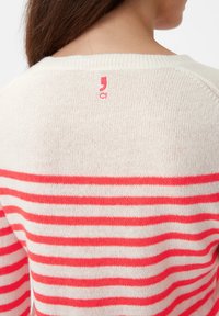 Gestreepte trui in crème en koraal, met een ronde halslijn en een klein logo in het rood op de achterkant. Gemaakt van zachte gebreide stof, met textuur.