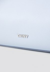 Lys blå teksturert syntetisk skinnveske med sølv DKNY-logo, minimalistisk design og kontrastfarge i mørkeblå detaljer.