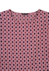 Top rosso con un motivo geometrico di cerchi sovrapposti in bianco e blu navy. Collo rotondo, maniche corte e texture liscia.