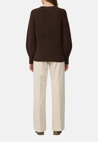 Brązowy sweter dzianinowy z raglanowymi rękawami, teksturowanym wzorem i ściągaczem u dołu, w połączeniu z kremowymi spodniami z szerokimi nogawkami.