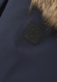 Marinblått tyg med en strukturerad yta, med en svart etikett med en logotyp och en pälsdetalj längs den övre kanten för extra detaljer.