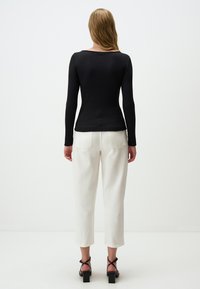 Zwarte geribbelde lange mouwen top in combinatie met witte crop pants en zwarte blokhak sandalen. Minimalistisch ontwerp, zachte textuur.