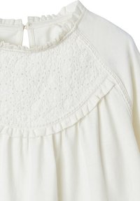 Weiße Bluse mit einem strukturierten Spitzenansatz, Rüschenausschnitt und gerafftem Stoff darunter. Weiches, leichtes Material mit einer glatten Oberfläche.