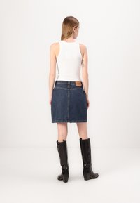 Jeans mini krilo s ravnim krojem, rahlo obrubljenim robom in usnjenim označevalcem na pasu. Nosi se z visokimi, sijajnimi črnimi čevlji.