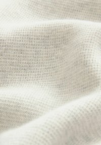 Cream-colored knit fabric with a fine texture, featuring a subtle pattern of interwoven fibers. Soft and slightly stretchy material.