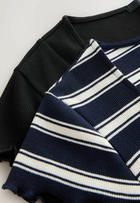 Két bordás felső: az egyik egyszínű fekete, a másik sötétkék fehér csíkokkal. Jellegzetes textúrájú anyag és aszimmetrikus szegélyek jellemzik.