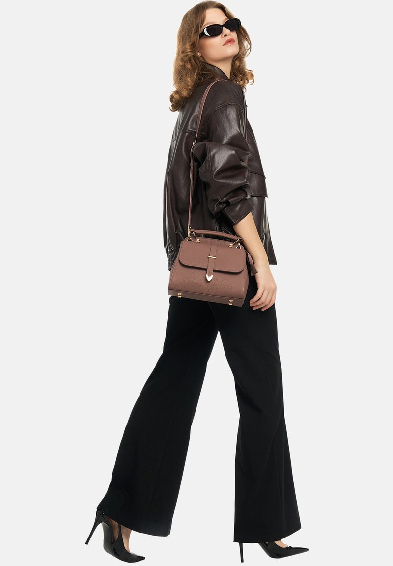 Woman wearing black sunglasses, brown leather jacket, black wide-leg pants, high heels, carrying a brown handbag over her shoulder.