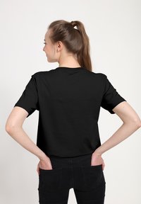 Černé bavlněné tričko s krátkými rukávy, kulatým výstřihem a hladkou strukturou, zobrazené zezadu, doplněné černými džínami.