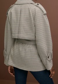 Geverifieerde stoffen jas met een cropped ontwerp, voorzien van een ceintuurlijn, knoopmanchetten en een gestructureerde kraag in neutrale tinten.