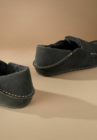 Tamsiai pilki zomšiniai slip-on tipo batai su minkštu kailių pamušalu, akcentu su kontrastinga siūle ir plokščiu guminio pado dizainu, užtikrinančiu komfortą.