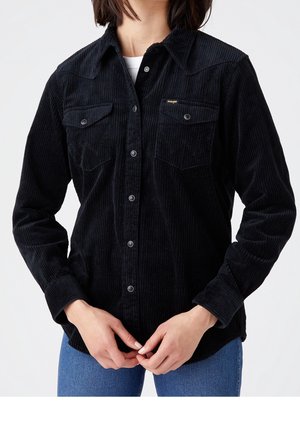 Black corduroy shirt with a button-up front, two chest pockets, and a textured fabric. Features a pointed collar and long sleeves.