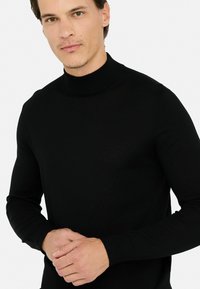 Maglione dolcevita nero realizzato in morbido tessuto a maglia, con un design aderente e polsini a coste. Costruzione semplice e senza cuciture.