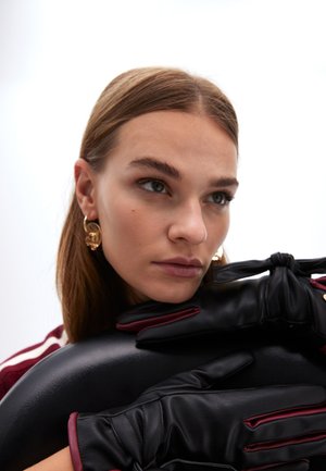 Guantes de cuero negro con acentos burdeos, que presentan un detalle de cinta anudada. La textura suave realza su diseño sofisticado.