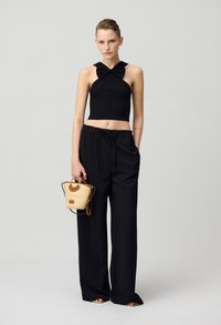 Zwarte geribbelde crop top met strikdetail, gecombineerd met losse zwarte broeken. Accessoire: kleine strooien tas met een bruin handvat. Platte sandalen.