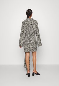 Schwarz-weiß gestreiftes Kleid im Zebramuster mit langen Ärmeln, tailliertem Schnitt und asymmetrischem Saum. Getragen mit schwarzen Blockabsatzschuhen.