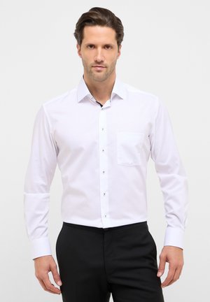 Weißes langärmeliges Hemd mit Knopfkragen, ausgestattet mit einer Brusttasche und schwarzen Knopfakzenten, kombiniert mit einer schwarzen Hose.