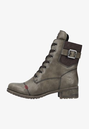 Stivale alla caviglia verde oliva realizzato in pelle texturizzata, con punta tonda, chiusura con lacci e una fibbia decorativa su un pannello marrone. Suola piatta in gomma con motivo.