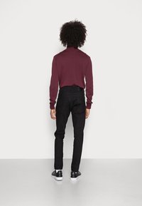 Camisa de manga larga en color burdeos combinada con jeans negros ajustados y zapatillas negras. Tejido suave con un diseño ajustado, simple y minimalista.