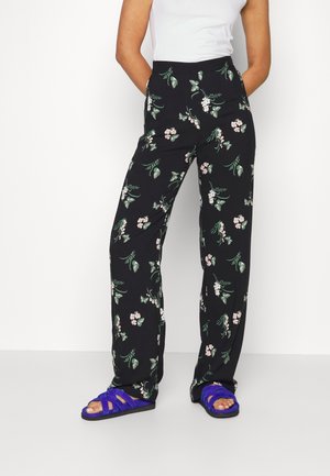 Woman wearing black floral wide-leg pants and purple open-toe sandals, paired with a sleeveless white top.