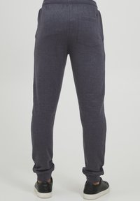 Dark gray tapered jogger pants made of a soft fabric. Features an elastic waistband and a back pocket. Paired with black sneakers.