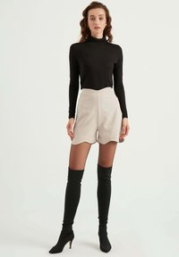 Zwarte langarm turtleneck, beige scalloped hoge taille shorts, zwarte thigh-high stiletto laarzen, gladde stof, aansluitend ontwerp.