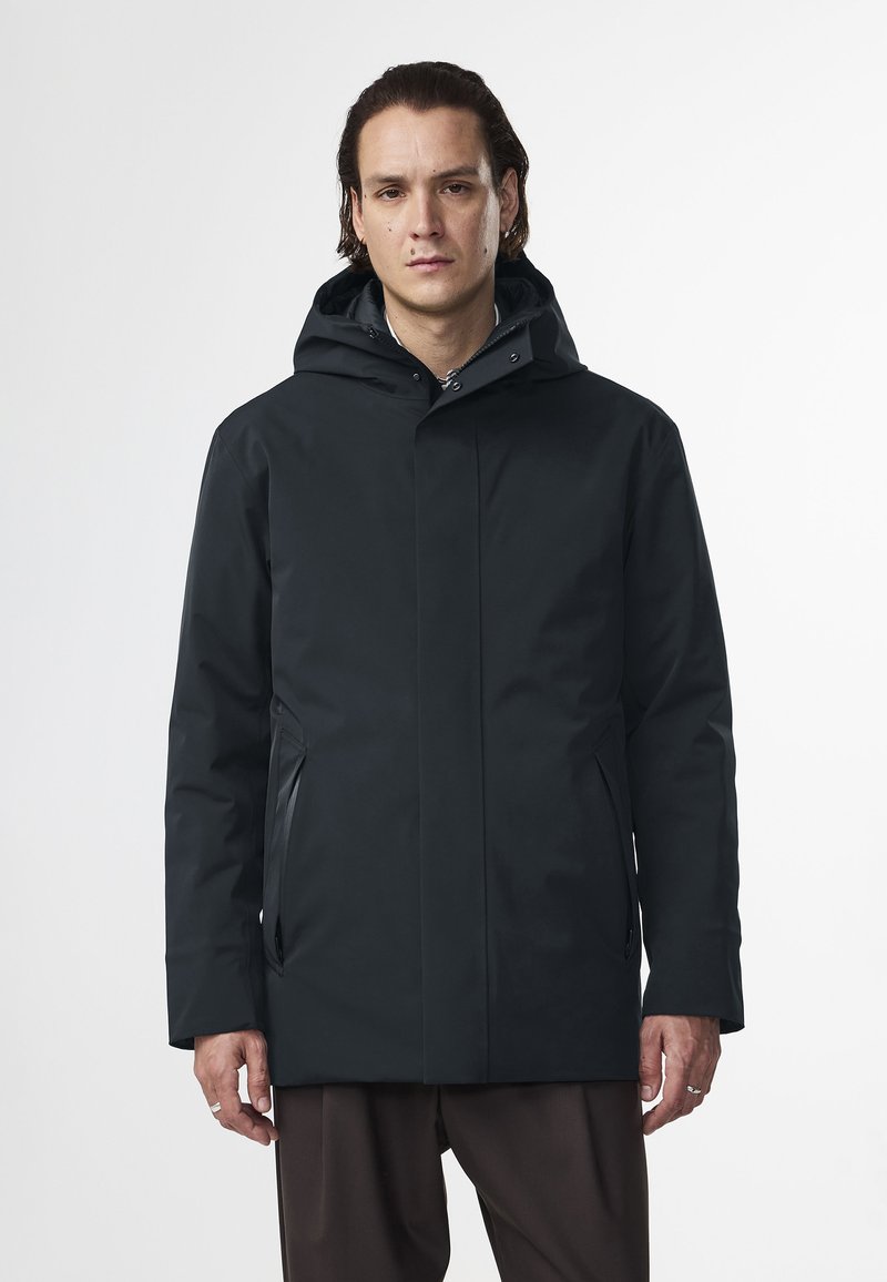 Giacca nera impermeabile con cappuccio, caratterizzata da un taglio dritto, due tasche laterali e una finitura opaca. Tessuto morbido con dettagli hardware minimi.