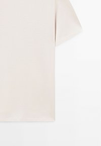 Short-sleeve, light beige t-shirt made of soft fabric, featuring a simple crew neck and a straight hem, with no visible patterns or accents.