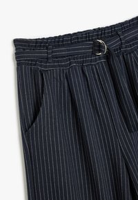 Marineblå bukser med lodrette hvide striber, udstyret med elastisk talje, bæltestropper og sidelommer. Tekstureret stof.