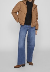 Brun puffjacka med hög krage, matchad med en svart texturerad stickad tröja och vida blå jeans. Bruna ankelboots fulländar looken.