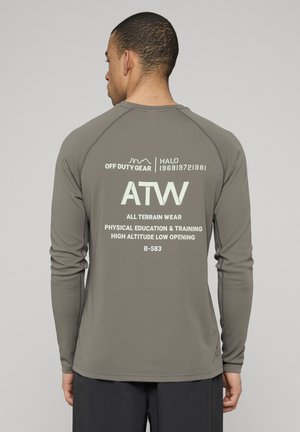 Grå träningsskjorta med långa ärmar och texturerad yta. Visar vit text på baksidan, inklusive varumärke och produktdetaljer.